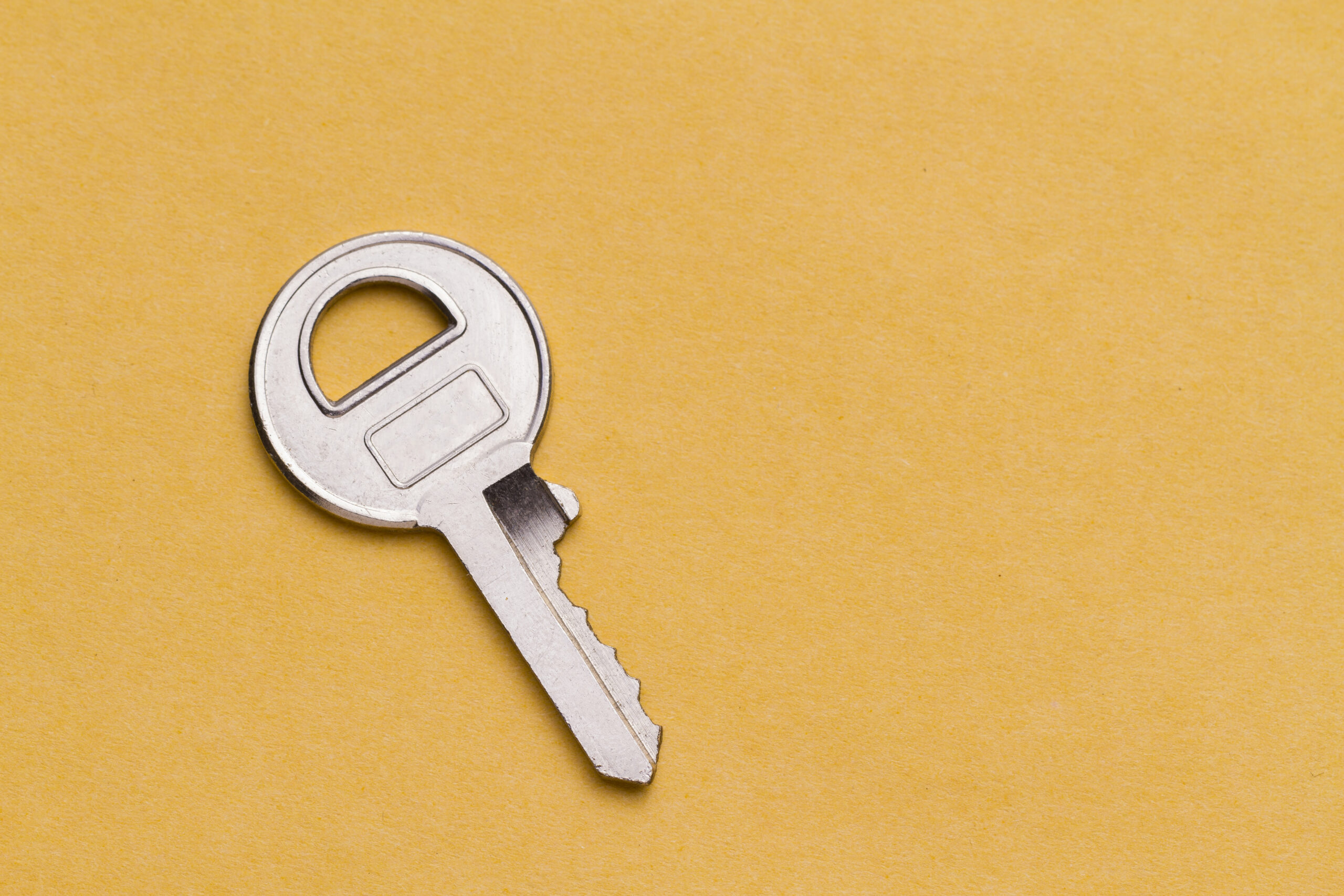 Small steel key on yellow background, space for text