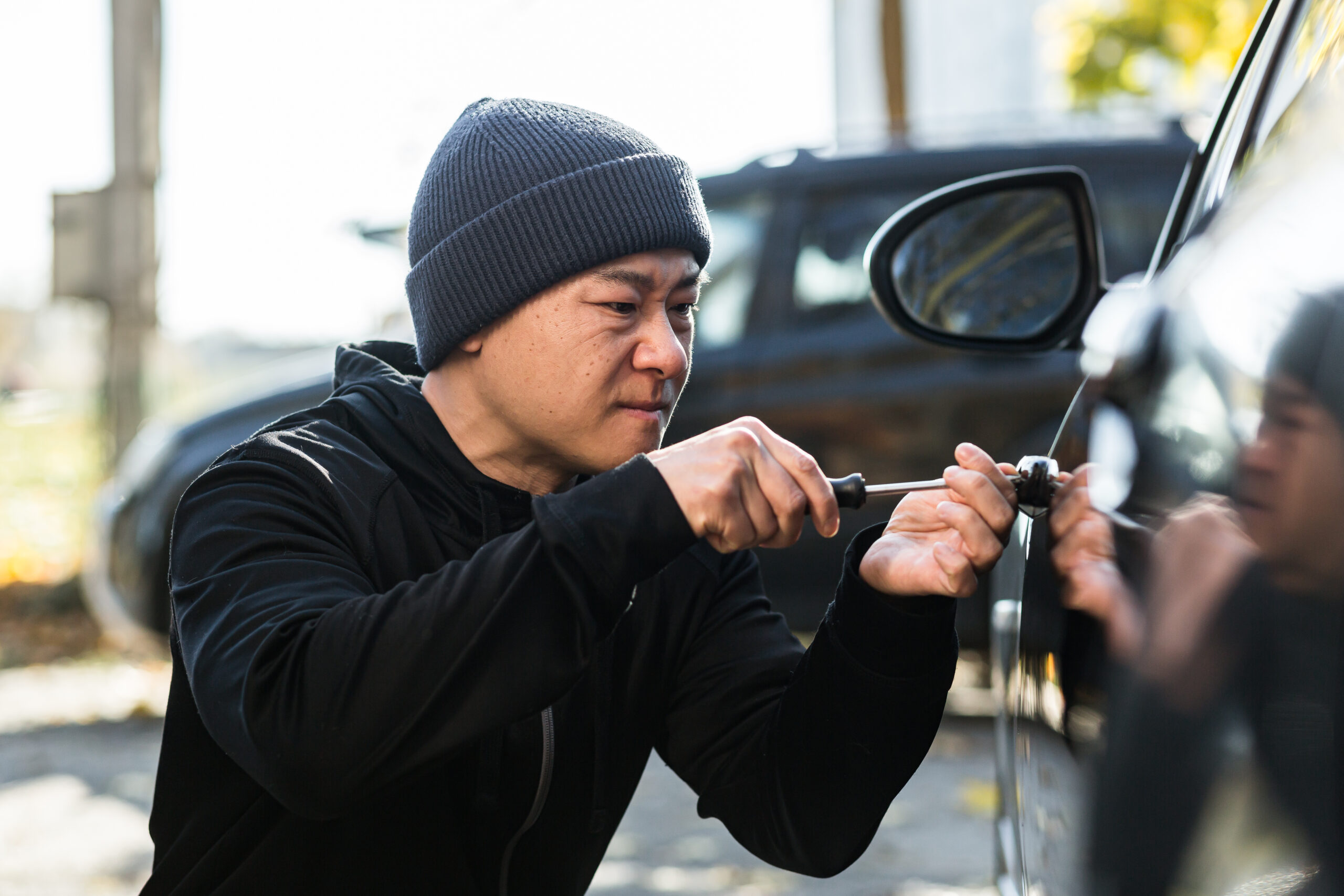 Male asian thief steals car breaks door lock with mechanical screwdriver tool